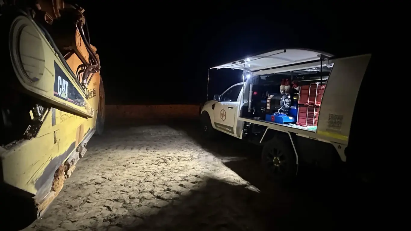 AHH mobile field workshop operating at night beside a CAT excavator